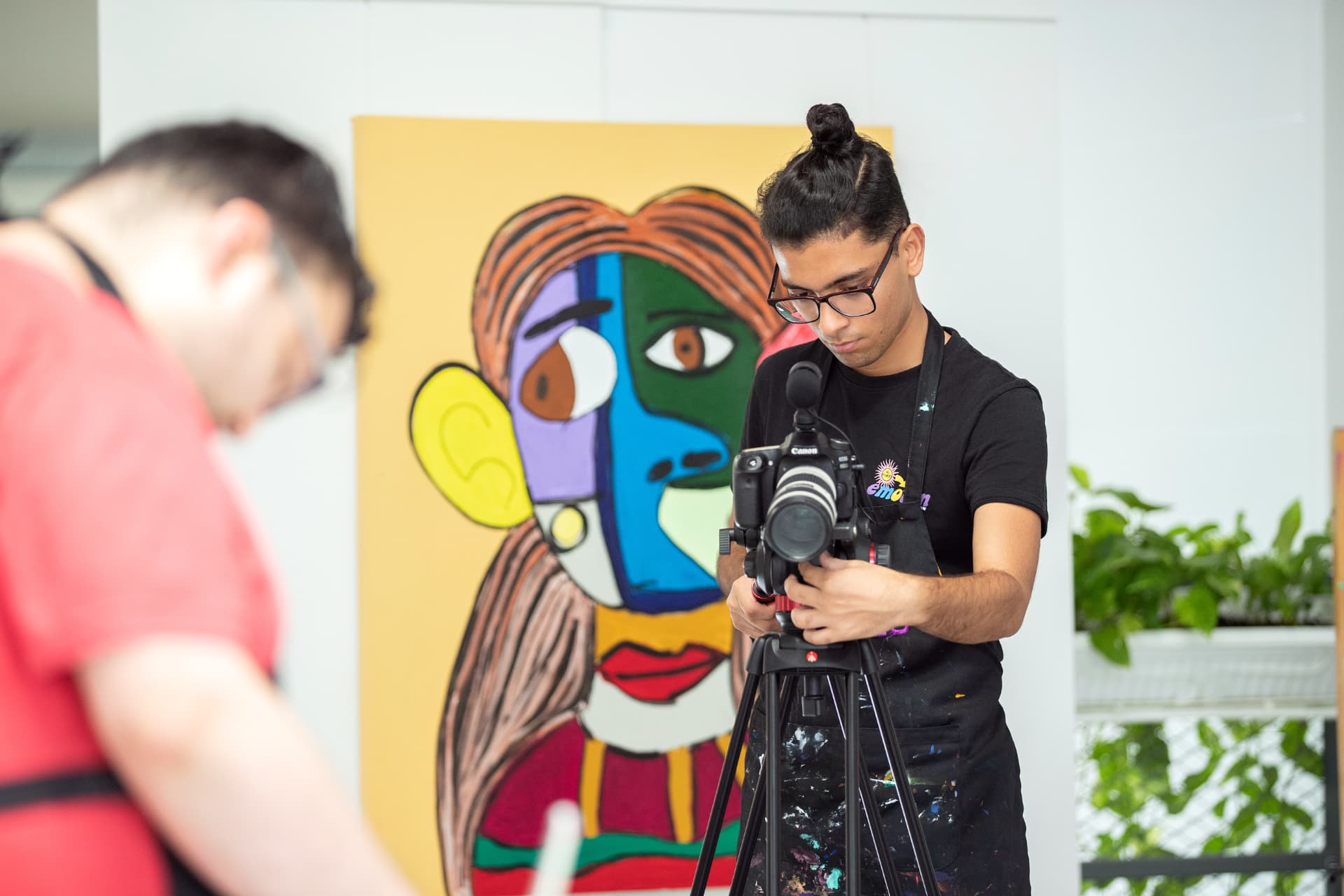 Ibad Hasan filming with a Canon camera on a tripod in an art studio