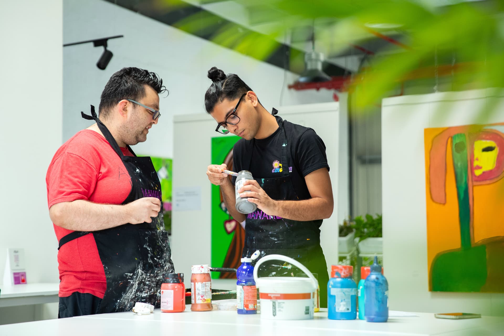 Ibad Hasan examining a jar of pigment beside a fellow artist in a studio workshop